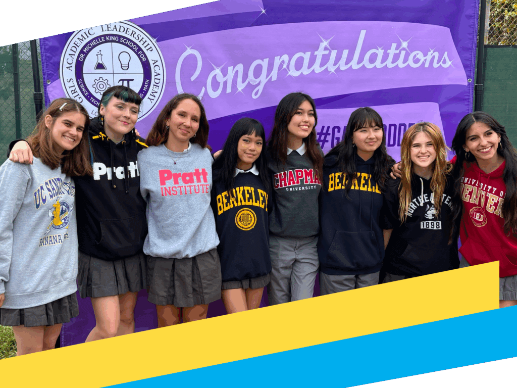 Eight students in school uniforms stand in front of a purple Congratulations banner, each wearing college or university sweatshirts, proudly celebrating girls education and their achievements, smiling with arms around each other.