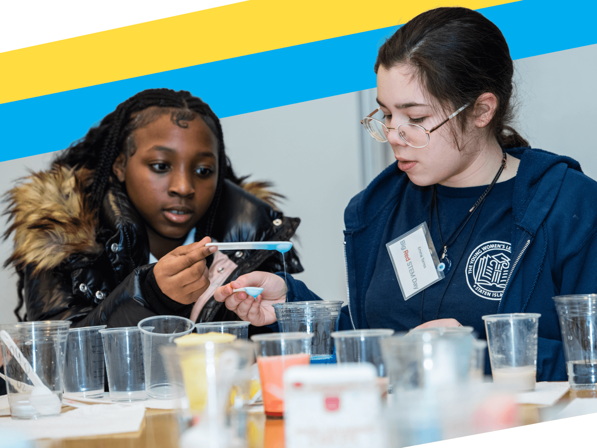 Two young women conduct a science experiment together, using pipettes and plastic cups on a table.
