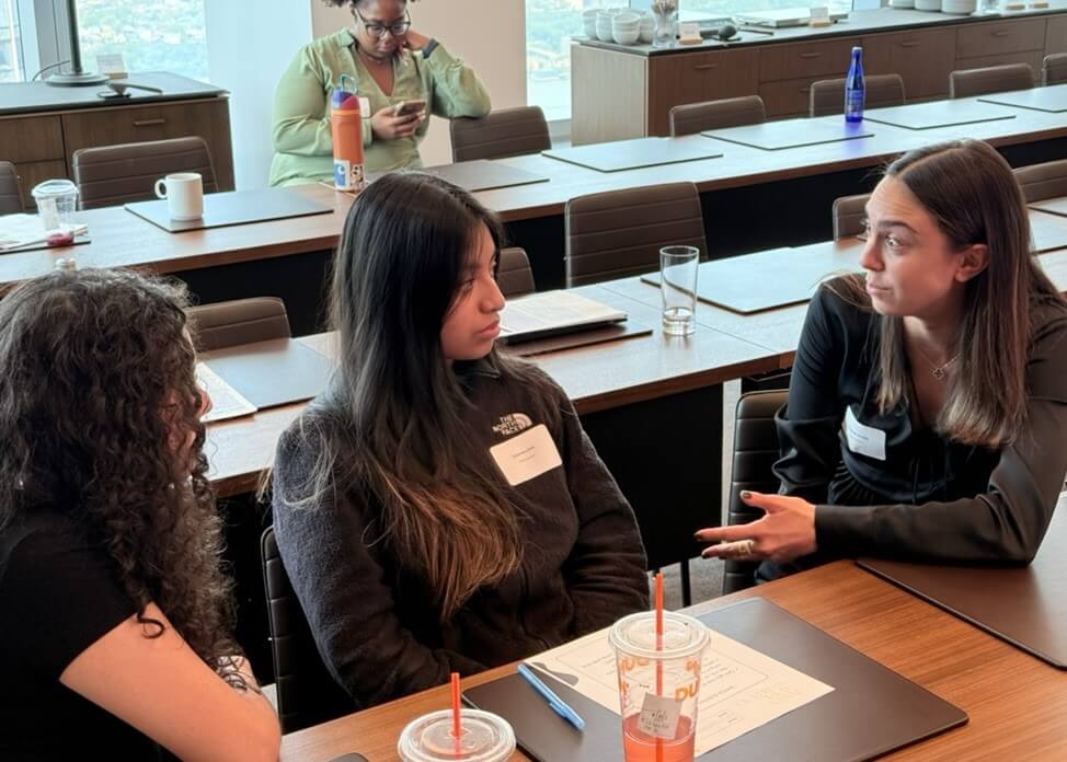 An adult and two students speak with each other in a conference room
