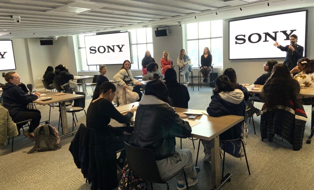 Several people sit at tables in a conference room, listening to a panel discussion in front of Sony-branded screens during the SUNY McConney EOP award presentation.