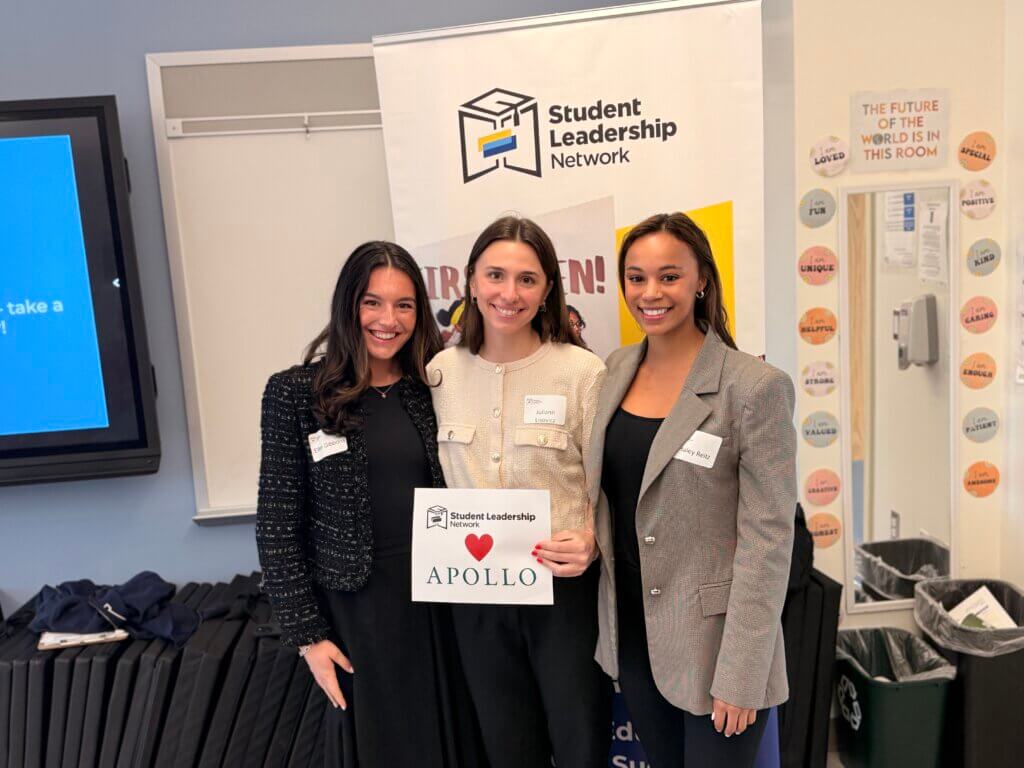 Three women stand indoors, smiling at the camera. One holds a sign that reads Student Leadership ❤️ Apollo. A Student Leadership Network banner behind them highlights the importance of early career exposure.