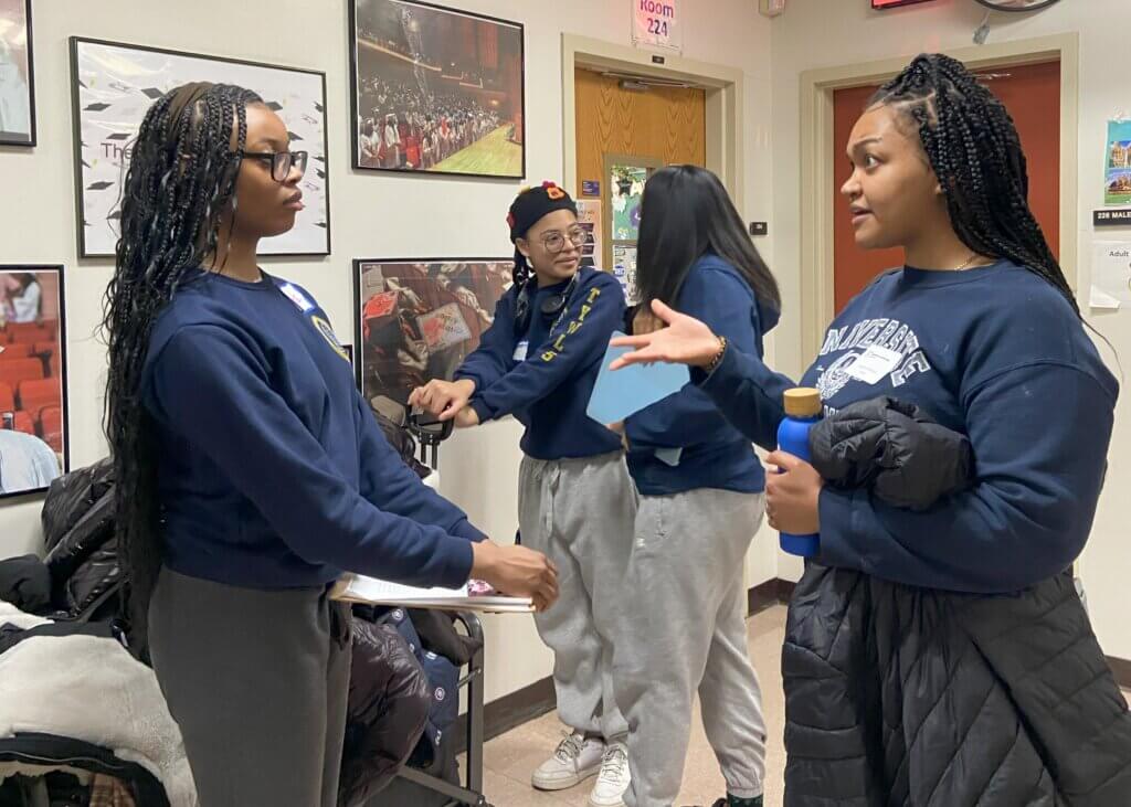 Four women stand in a hallway engaged in conversation