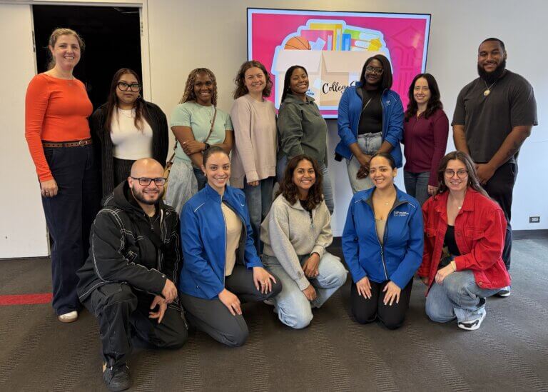 A group of thirteen people pose for a photo indoors in front of a screen displaying a colorful graphic celebrating collegebridge support for transition from high school to college.