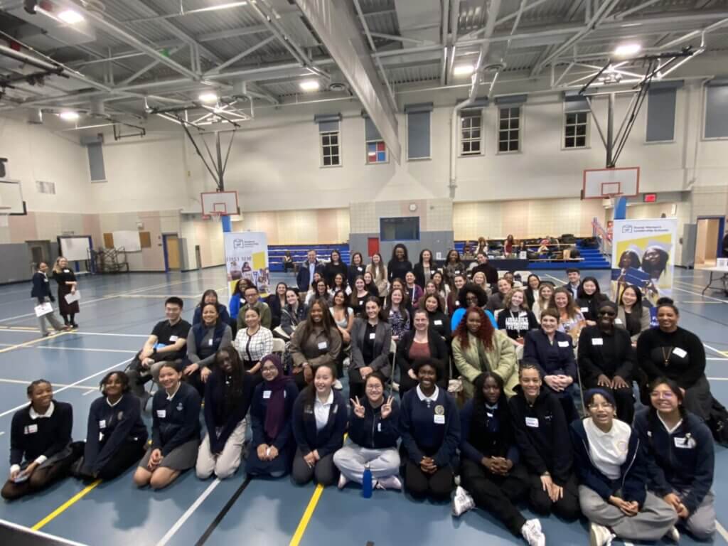 A large group of students and adult volunteers pose for a group photo in a gymnasium