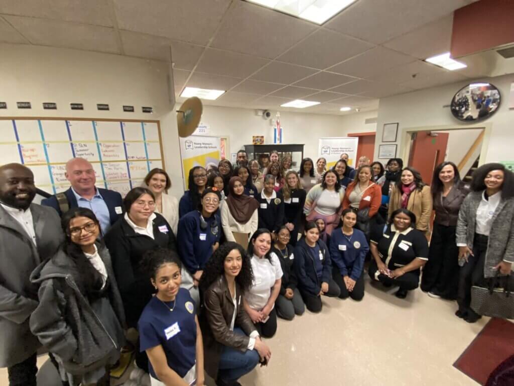 A large group of students and adult volunteers pose together in a school hallway