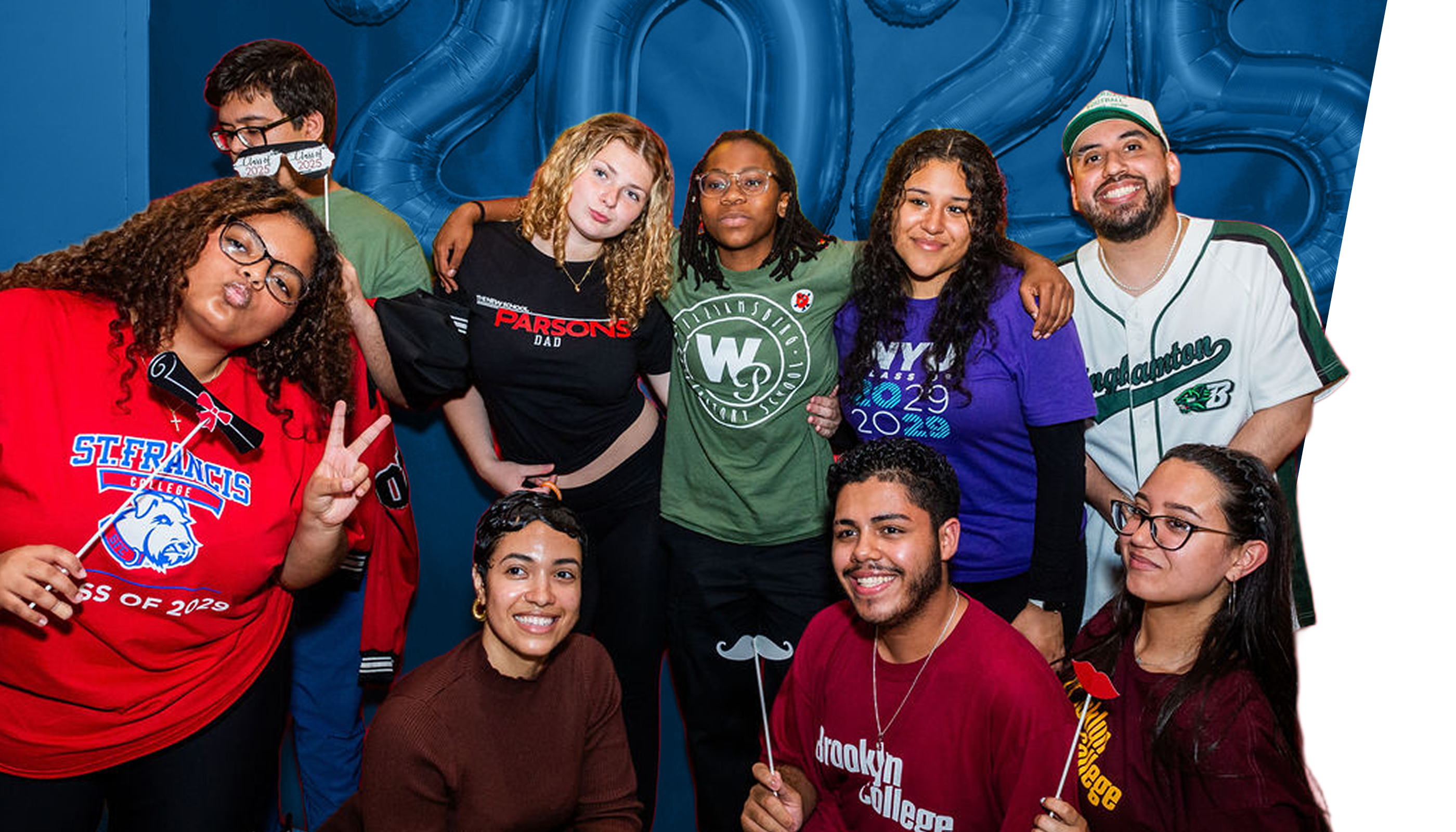 A group of nine young people pose and smile in front of gold balloons spelling “2025” with a red backdrop, some holding props and wearing college or class year shirts, celebrating their collegebridge support for transition from high school to college.
