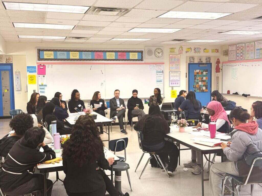 A group of students and panelists sit in a classroom, participating in a discussion.