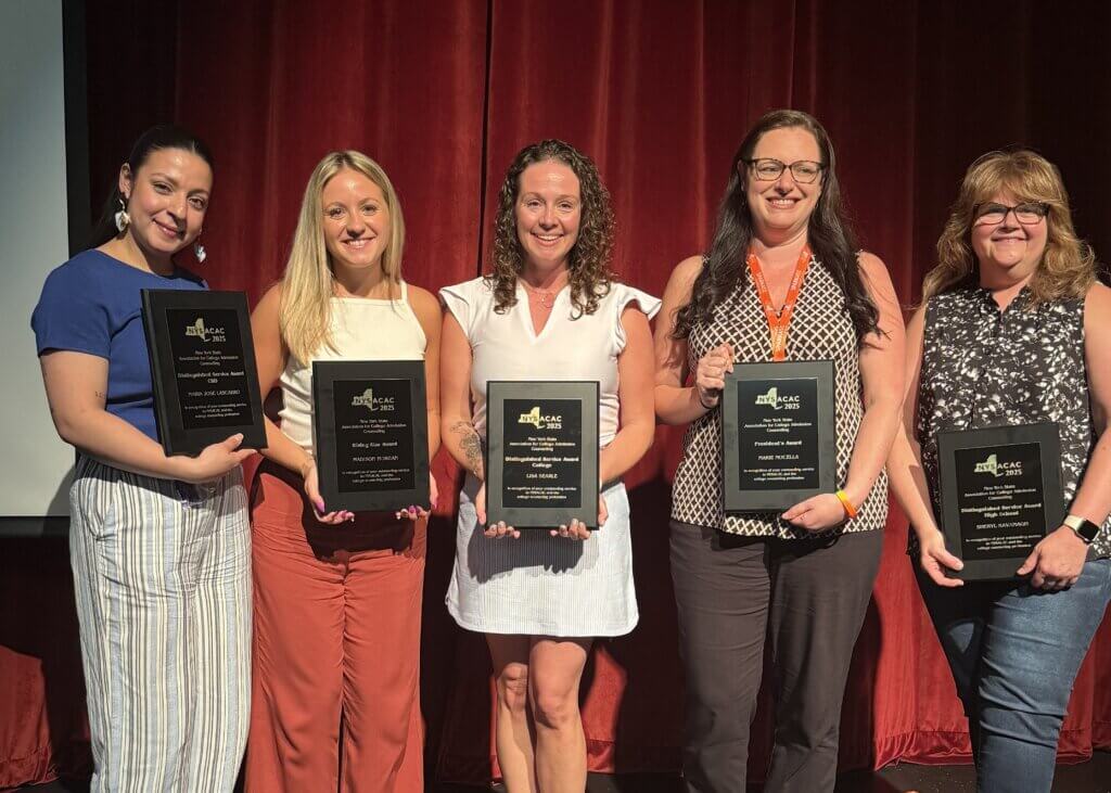 Five women stand in front of a red curtain, each holding a black plaque award and smiling at the camera.