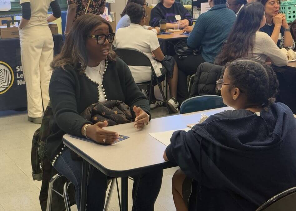 Two people sit at a table engaged in conversation in a busy indoor setting