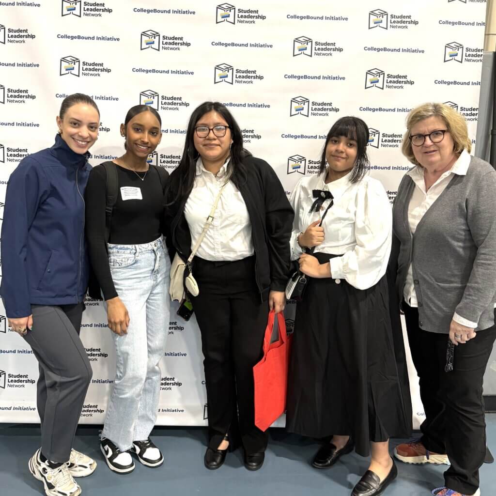 Students smiling stand in front of a CollegeBound Initiative step-and-repeat banner