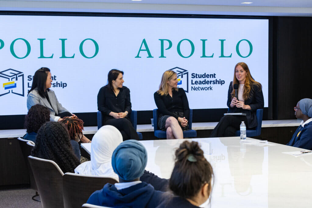Four women sit on a panel speaking to an audience in a conference room, with APOLLO and Student Leadership Network displayed on screens behind them.
