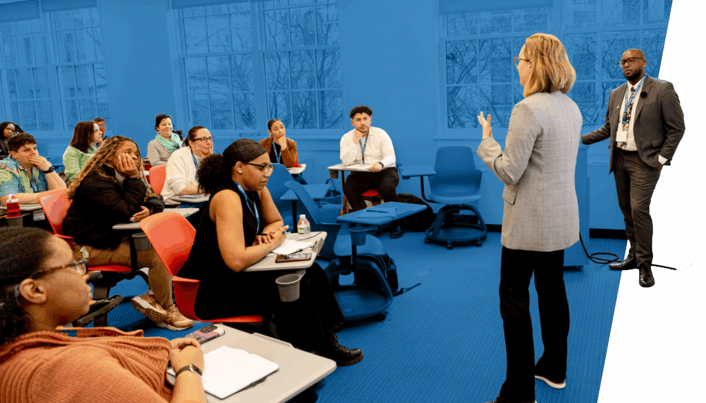 Student Leadership Network team members stand and speak to a seated classroom of educators and school administrators who listen and take notes.