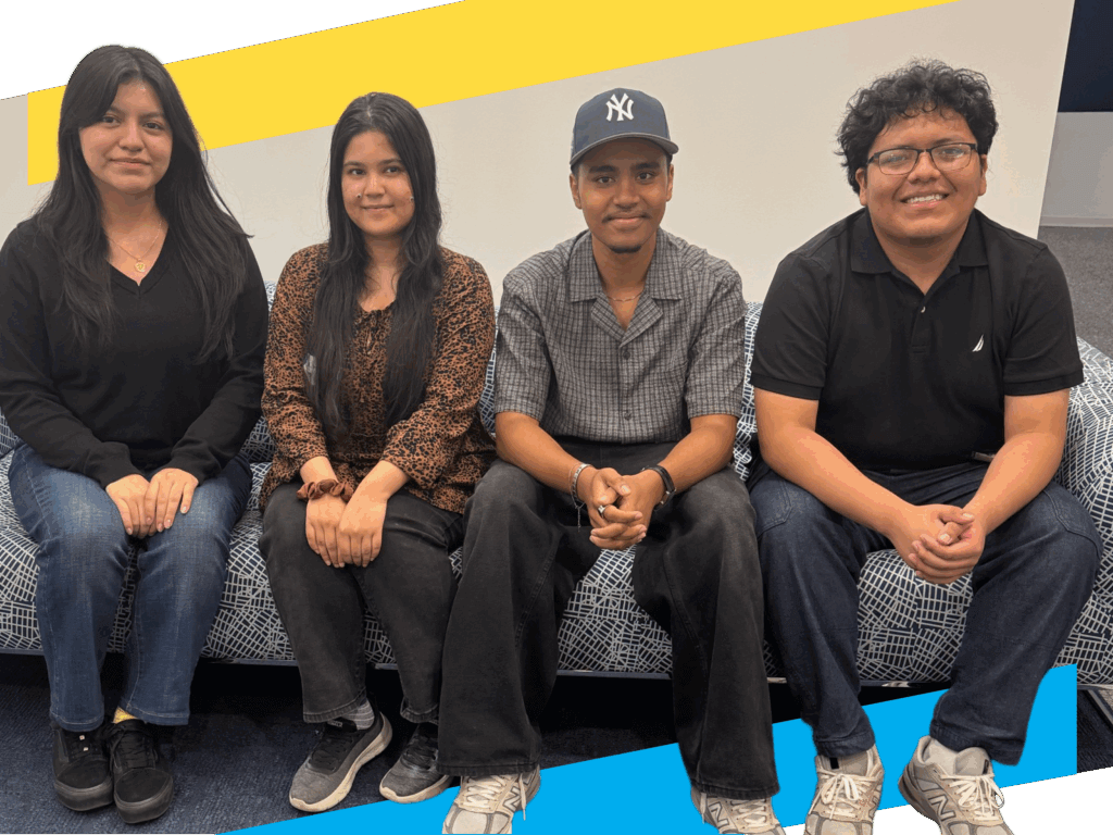 Four people are sitting on a patterned blue sofa against a plain white wall, looking at the camera and smiling.
