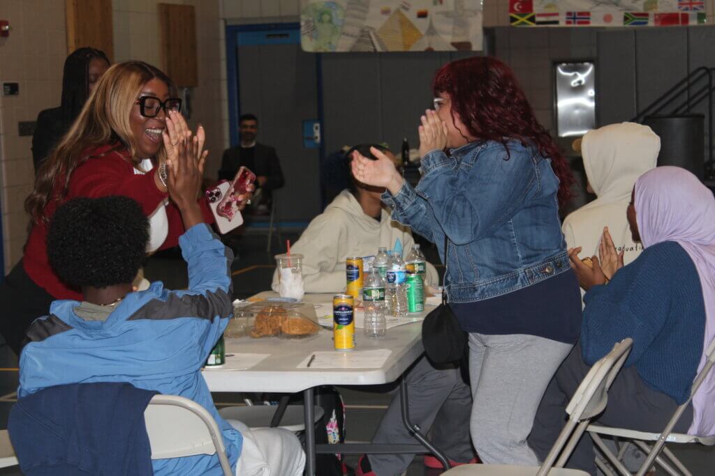 Two women standing at a table give each other a high five, surrounded by seated people