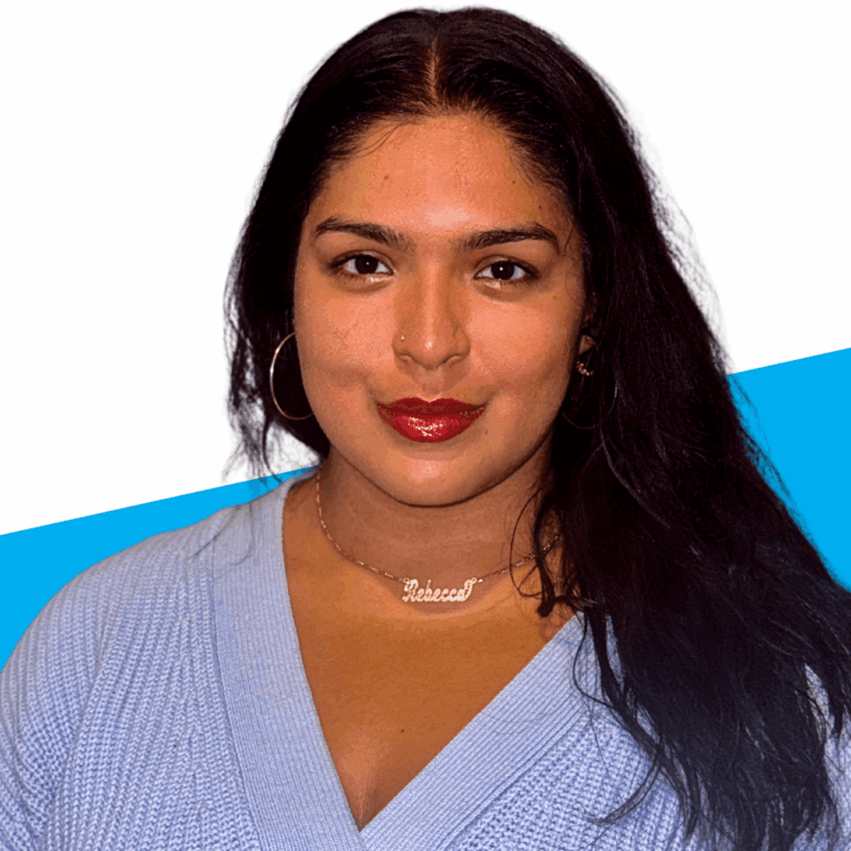 A person with long dark hair, wearing hoop earrings, a necklace that says Rebecca Herrera, and a light purple sweater against a white and blue background.